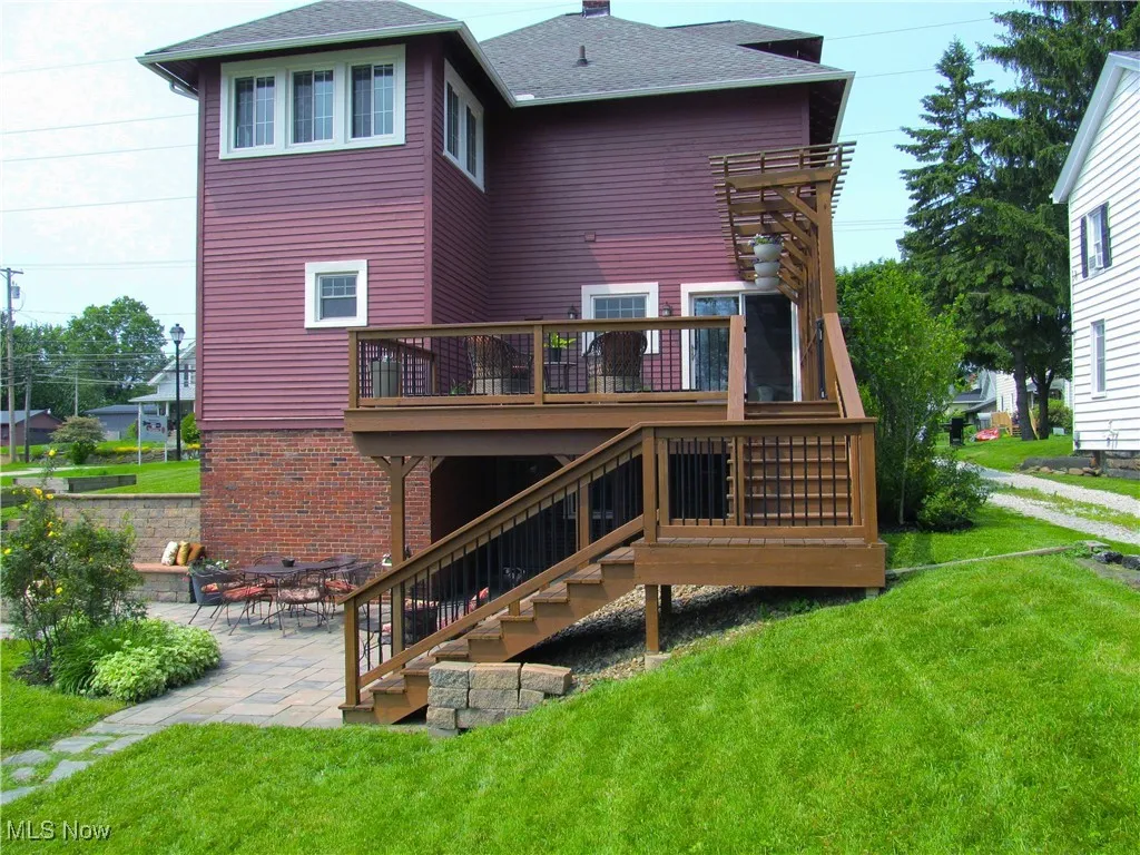 Rear view of property featuring a deck, stairs, a chimney, and a lawn
