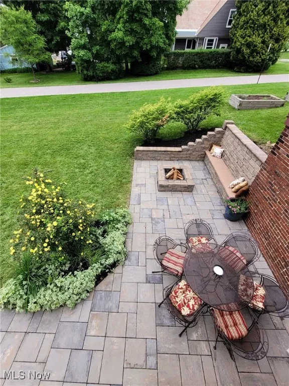 View of grassy yard featuring an outdoor fire pit and a patio area