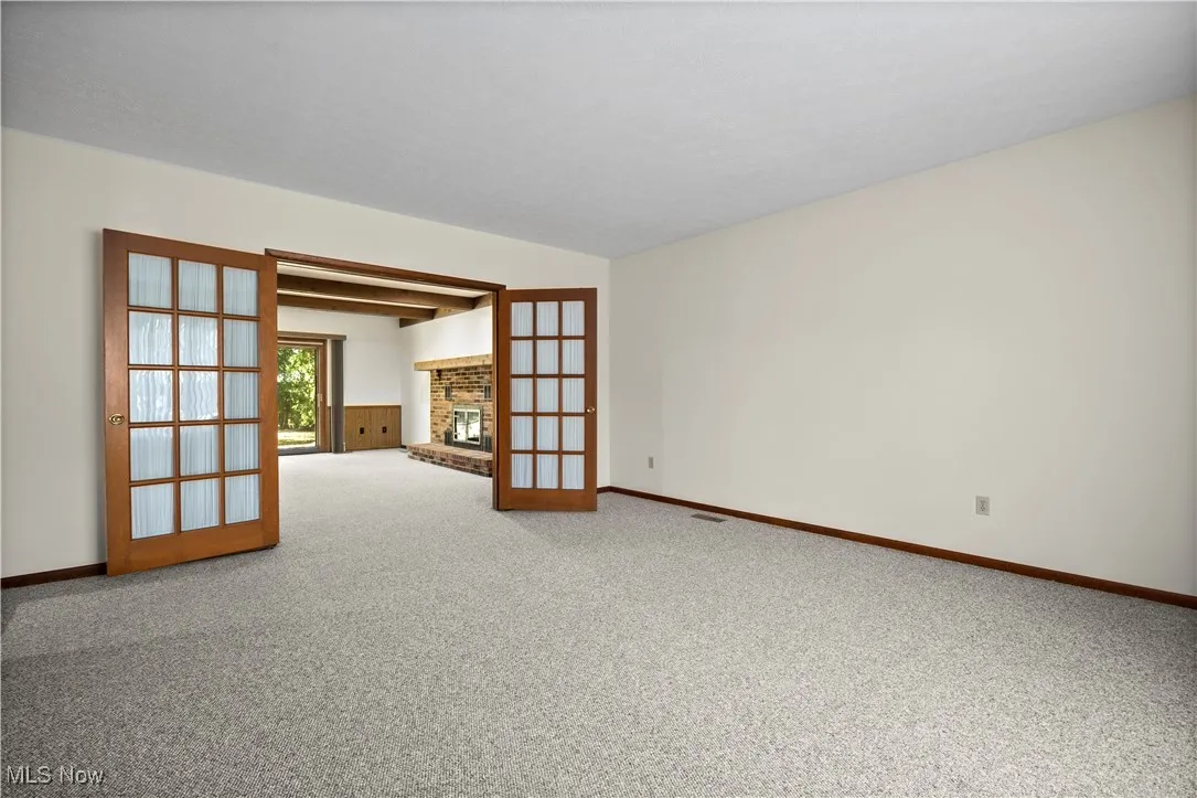 Unfurnished room with light carpet, a brick fireplace, and french doors