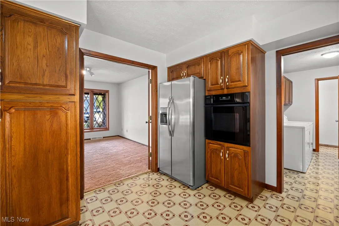 Kitchen with a textured ceiling, oven, stainless steel refrigerator with ice dispenser, washer / clothes dryer, and brown cabinetry
