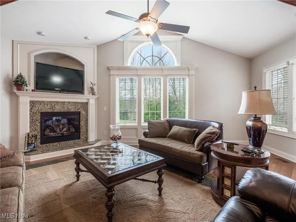 Living room with lofted ceiling, a ceiling fan, a premium fireplace, and wood finished floors