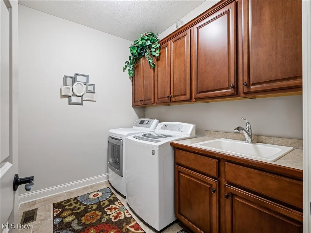 Washroom with washer and clothes dryer, light tile patterned floors, cabinet space, and a textured ceiling