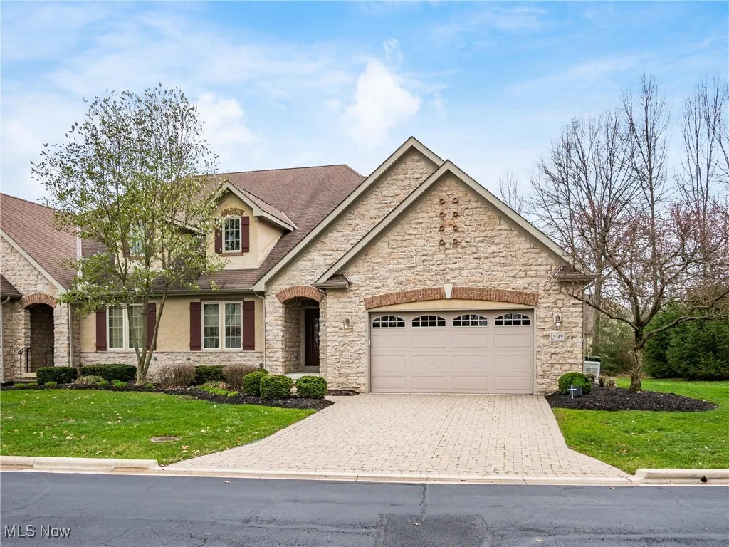 View of front of house with stone siding, a front yard, and decorative driveway