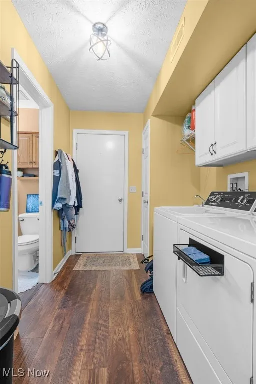Laundry room with cabinet space, a textured ceiling, dark wood-type flooring, and washing machine and clothes dryer