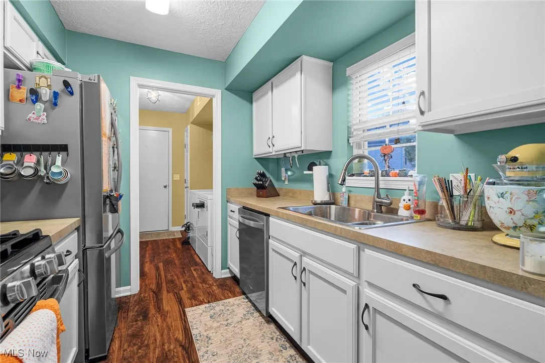 Kitchen with white cabinets, dark wood finished floors, appliances with stainless steel finishes, light countertops, and a textured ceiling