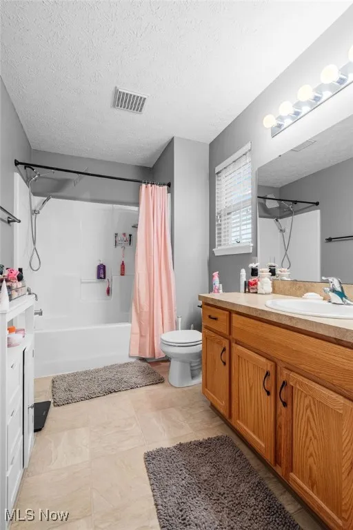 Bathroom with vanity, shower / tub combo, a textured ceiling, and light tile patterned floors