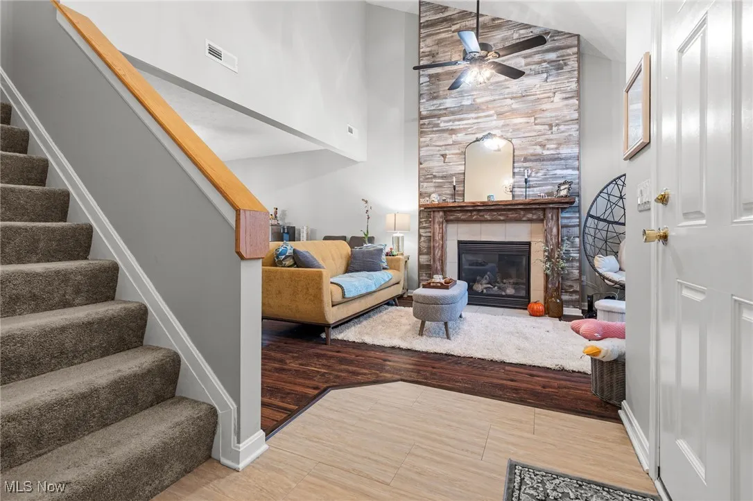 Living area featuring stairway, a fireplace, light wood-style flooring, high vaulted ceiling, and a ceiling fan
