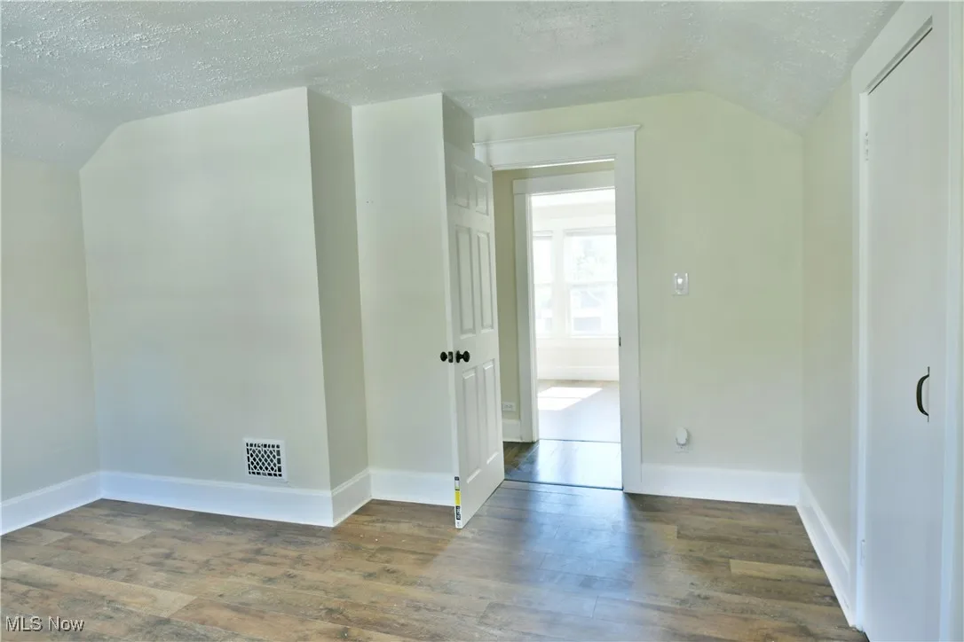 Bonus room with a textured ceiling, dark wood-style flooring, and lofted ceiling