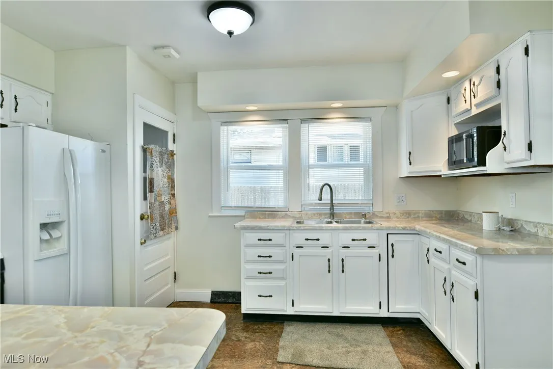 Kitchen with white cabinetry, white fridge with ice dispenser, light countertops, black microwave, and recessed lighting