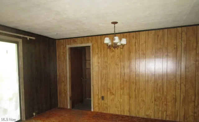 Unfurnished dining area featuring a chandelier and wood walls