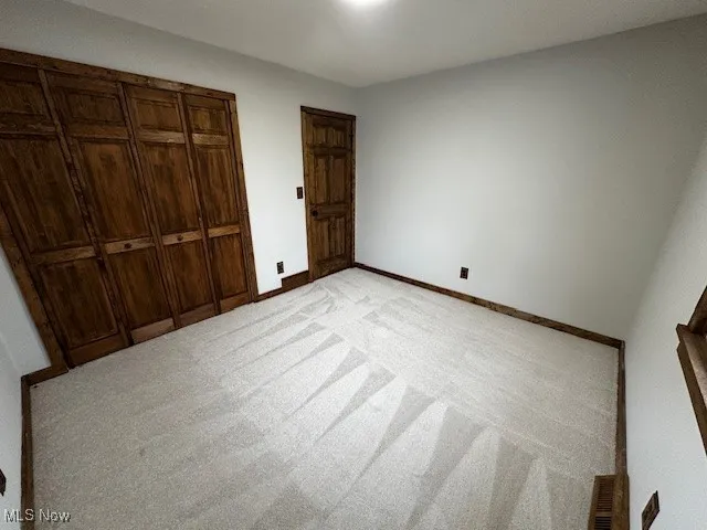 Unfurnished bedroom featuring light carpet and a closet