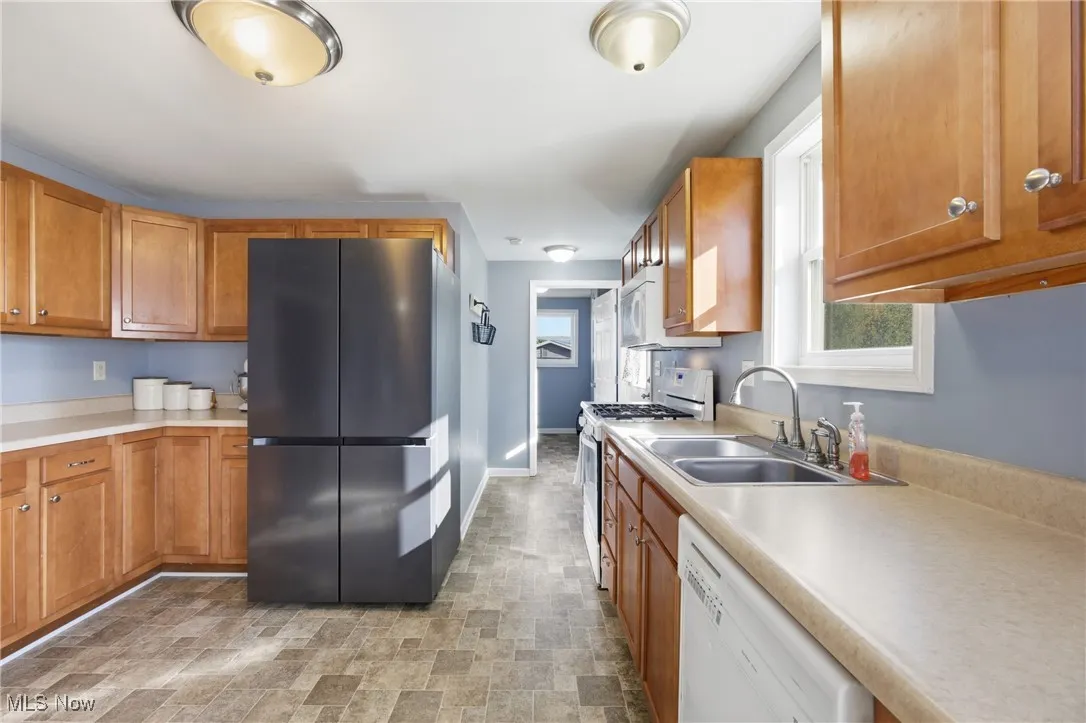 Kitchen featuring stainless steel appliances, brown cabinets, light countertops, and stone finish floors