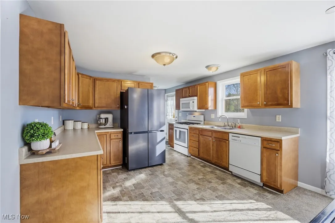 Kitchen featuring light countertops, white appliances, brown cabinets, and stone finish floors