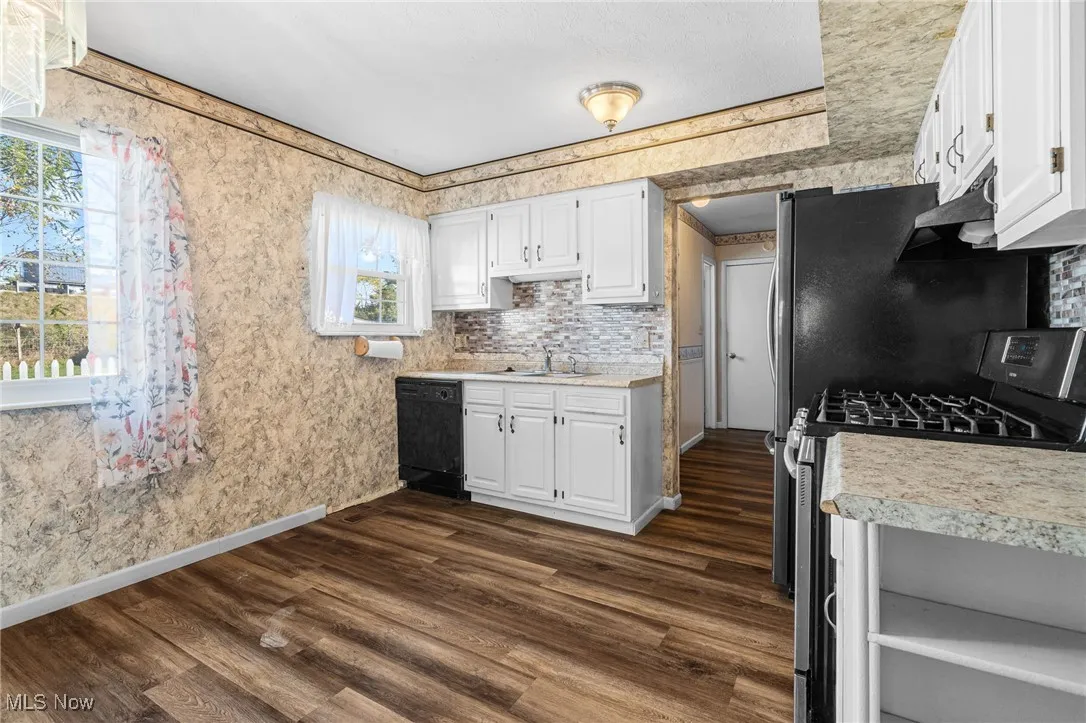 Kitchen featuring stainless steel range with gas stovetop, white cabinetry, dark wood-style floors, and wallpapered walls