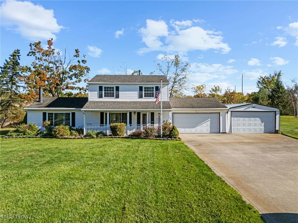 Traditional-style home with covered porch, a front yard, driveway, an attached garage, and a shingled roof