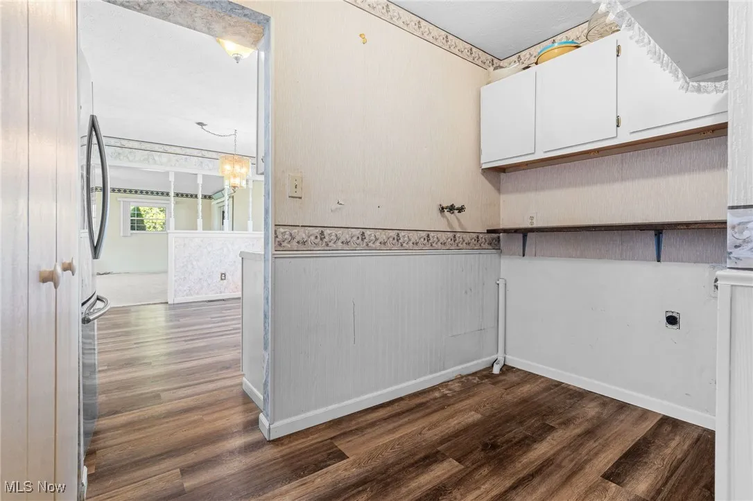 Washroom with wallpapered walls, dark wood finished floors, cabinet space, electric dryer hookup, and a chandelier