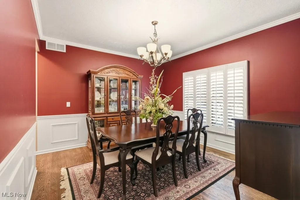 Dining room featuring light wood finished floors, crown molding, a chandelier, and wainscoting