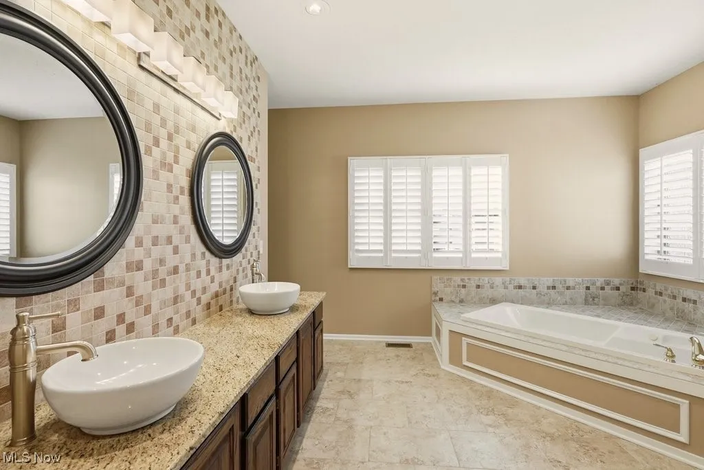 Full bath featuring a bath, double vanity, decorative backsplash, and light tile patterned floors