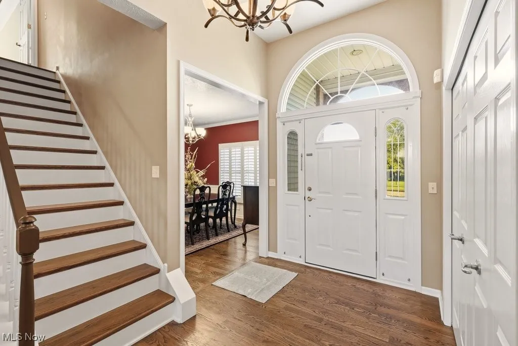 Entrance foyer with a chandelier, dark wood-style floors, and stairs
