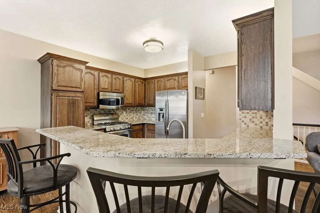 Kitchen featuring a kitchen bar, appliances with stainless steel finishes, tasteful backsplash, brown cabinets, and a peninsula