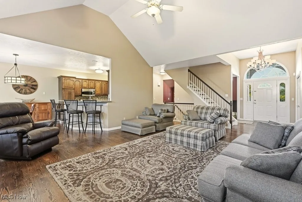 Living area with dark wood-type flooring, high vaulted ceiling, a ceiling fan, stairs, and a chandelier