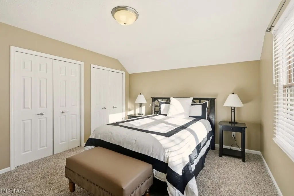 Bedroom with two closets, vaulted ceiling, and light colored carpet