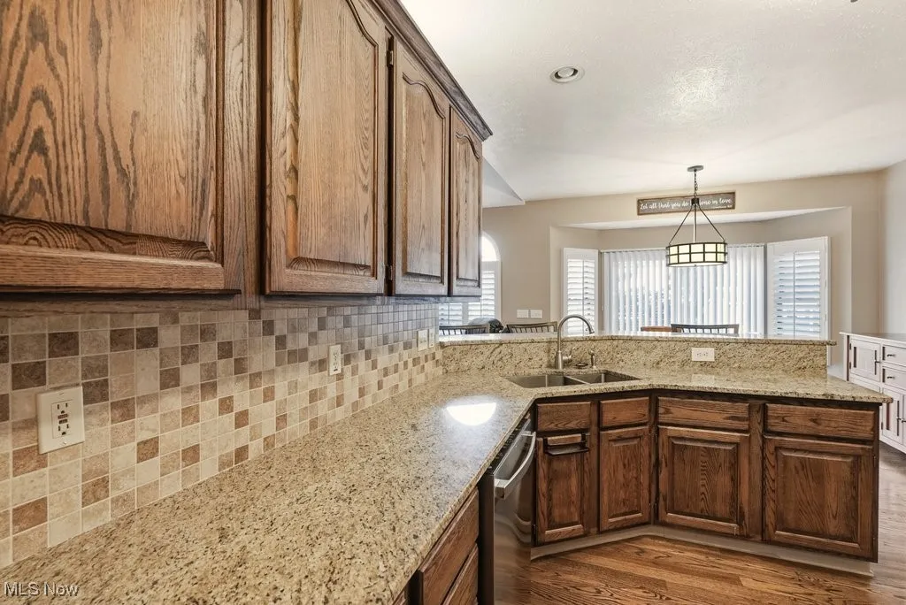 Kitchen featuring a peninsula, backsplash, light stone counters, dark wood-type flooring, and dishwasher