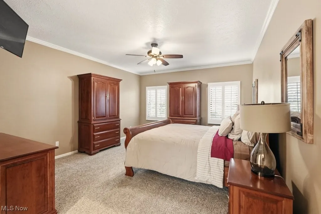 Bedroom with light carpet, ornamental molding, ceiling fan, and a textured ceiling