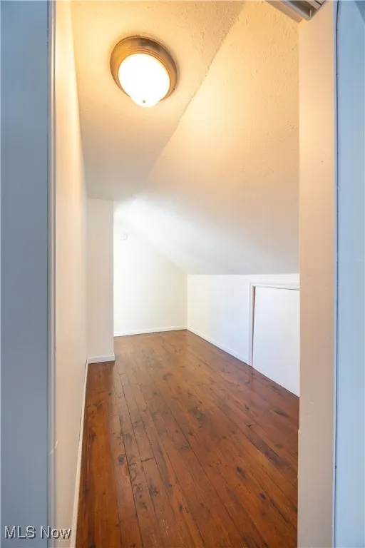 Additional living space with dark wood-style floors, vaulted ceiling, and a textured ceiling