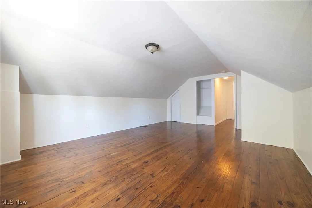 Additional living space featuring dark wood-style flooring and lofted ceiling