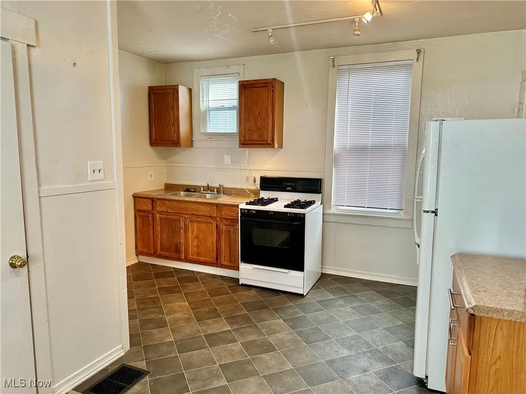 Kitchen featuring gas stove, freestanding refrigerator, brown cabinetry, and light countertops