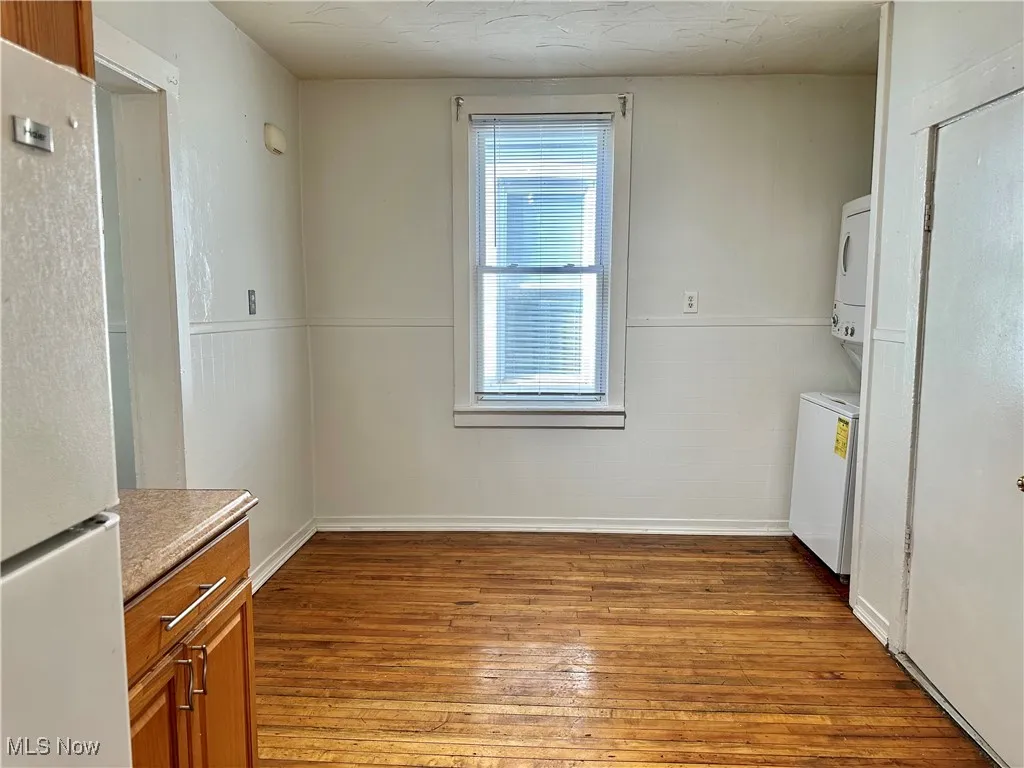 Unfurnished dining area with light wood finished floors, stacked washer and clothes dryer, and a wainscoted wall
