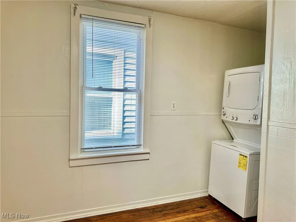 Laundry room with a wainscoted wall, dark wood-type flooring, stacked washing machine and dryer, and tile walls