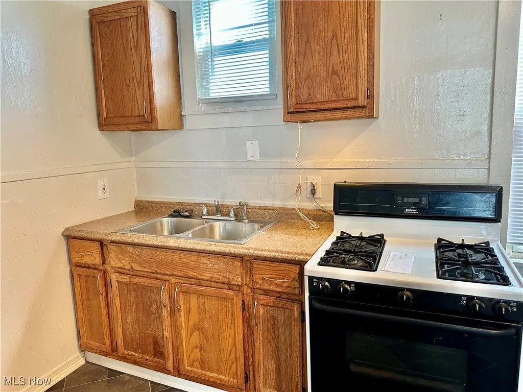 Kitchen featuring black range with gas stovetop, brown cabinets, light countertops, and dark tile patterned floors