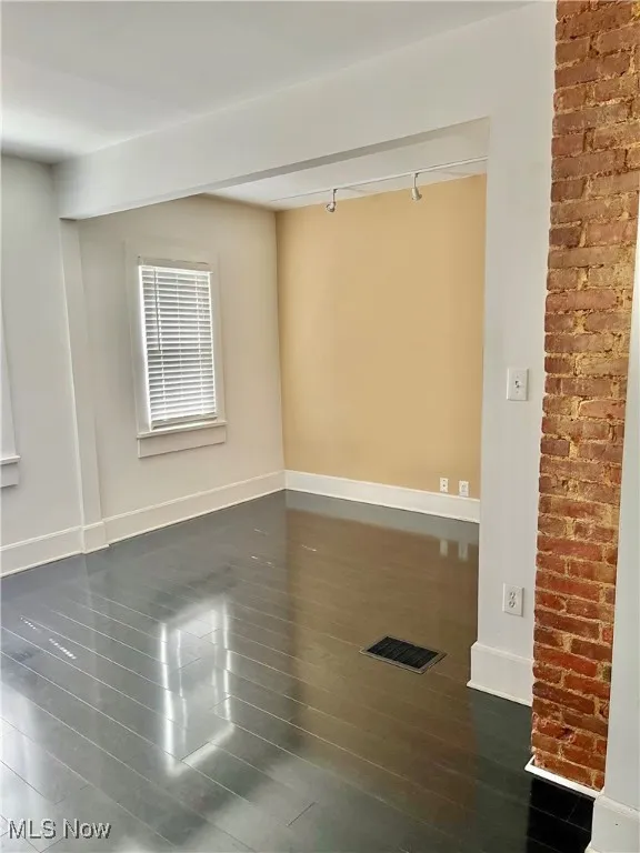 Empty room with track lighting and dark wood-style flooring
