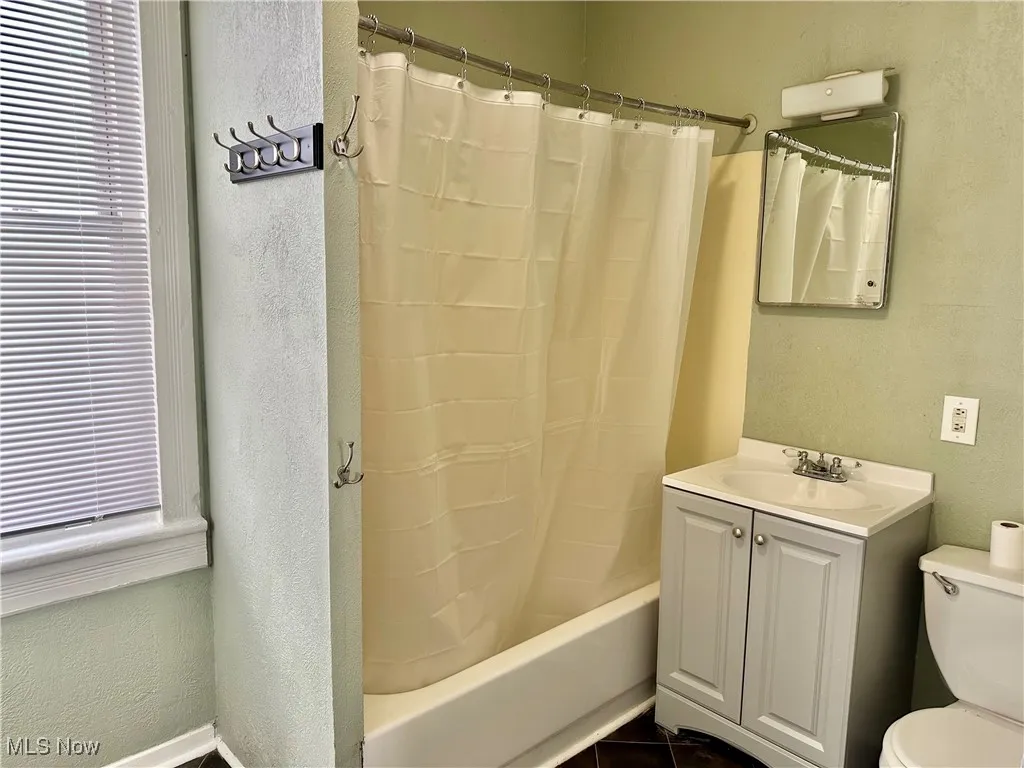 Full bath with a textured wall, plenty of natural light, vanity, and shower / bath combo