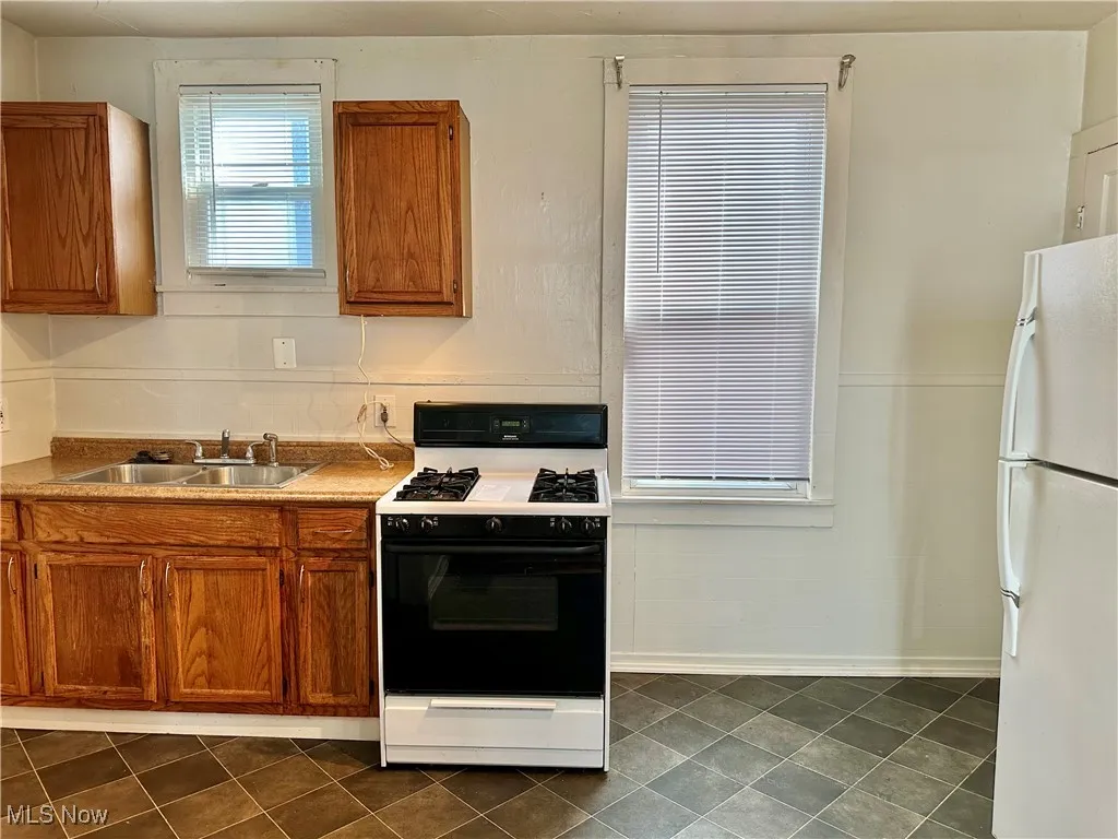 Kitchen with gas range, freestanding refrigerator, brown cabinetry, and light countertops