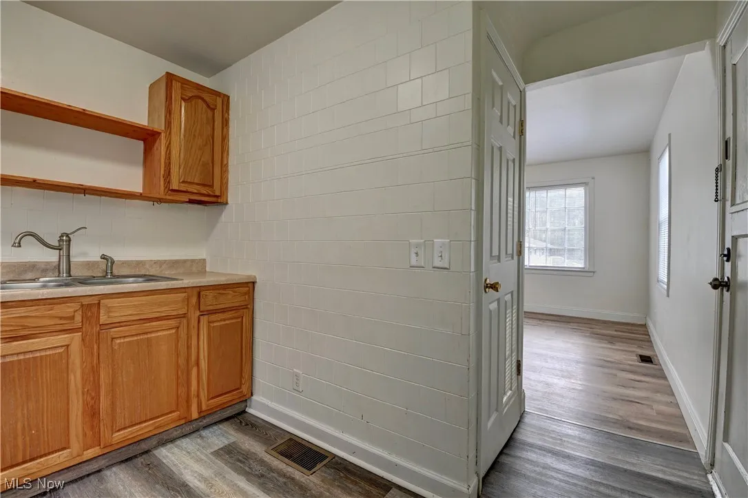 Kitchen featuring dark wood-style flooring, light countertops, brown cabinets, tile walls, and open shelves