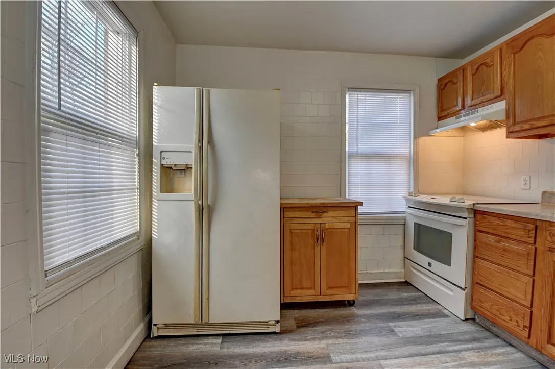 Kitchen featuring white appliances, dark wood-style floors, light countertops, under cabinet range hood, and brown cabinetry