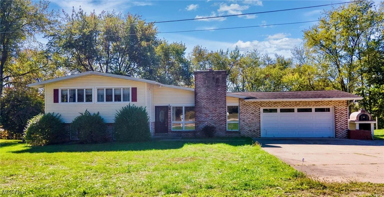 Split level home featuring brick siding, a front lawn, concrete driveway, a chimney, and an attached garage