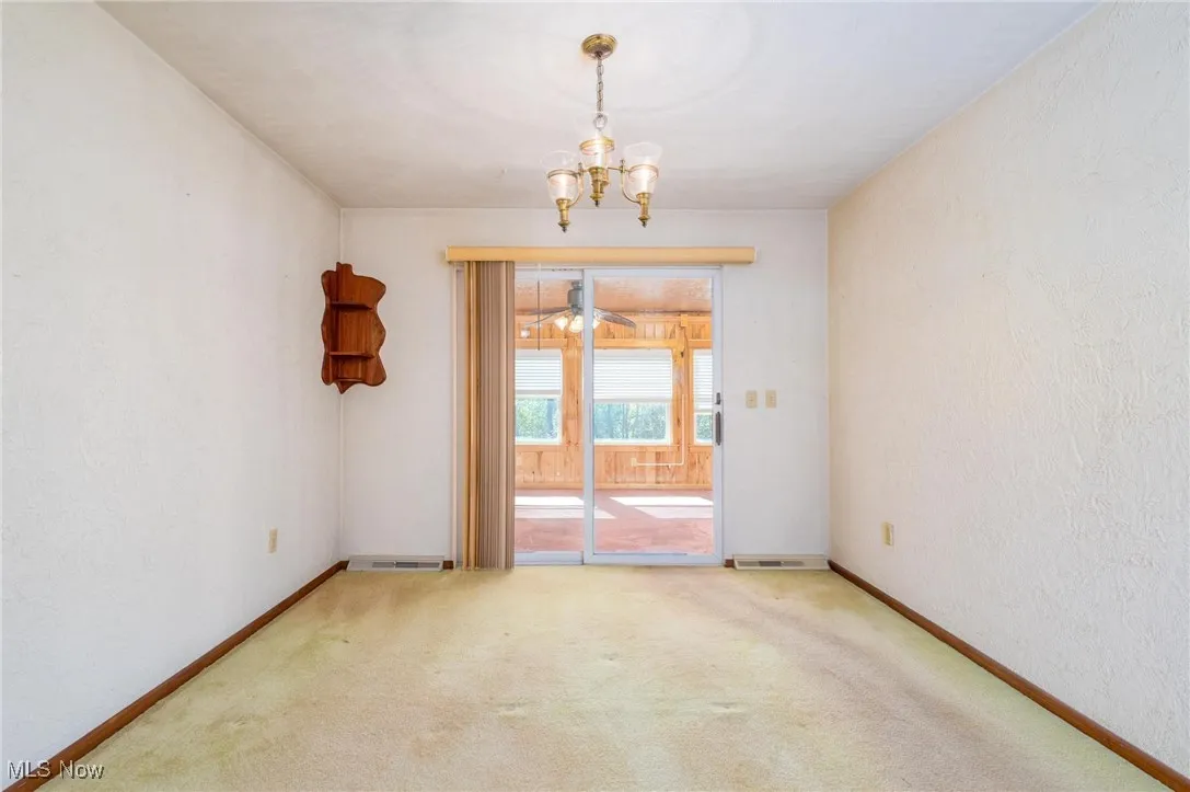 Empty room with a textured wall, light carpet, and a chandelier