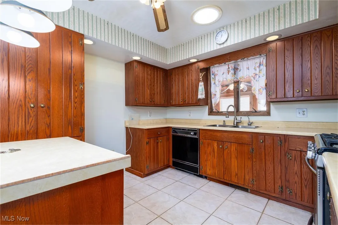 Kitchen featuring stainless steel gas stove, light tile patterned floors, light countertops, black dishwasher, and a ceiling fan