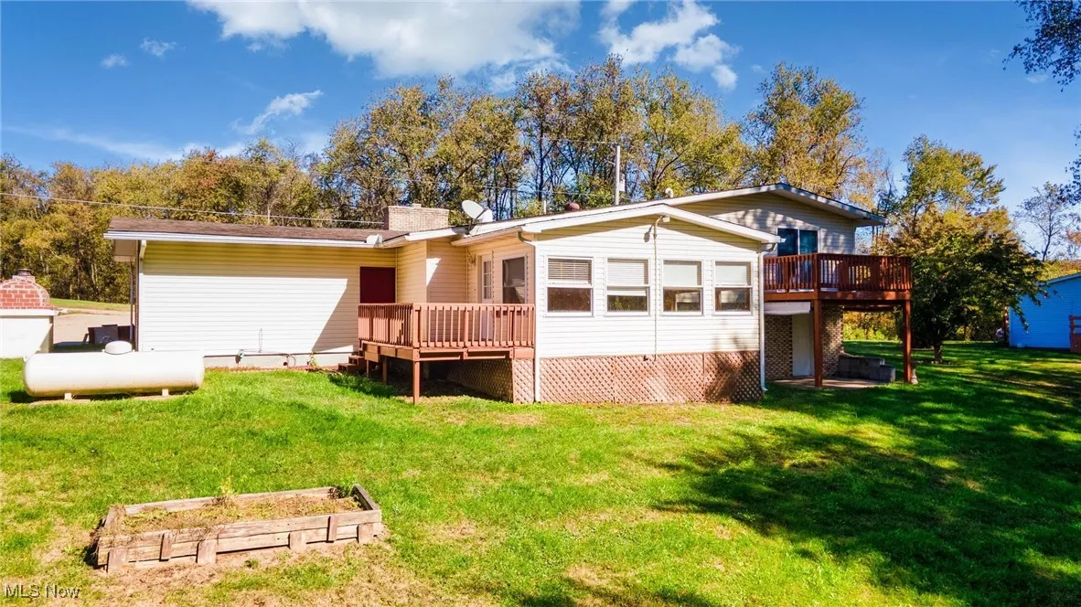 Back of property featuring a deck, a lawn, and a garden