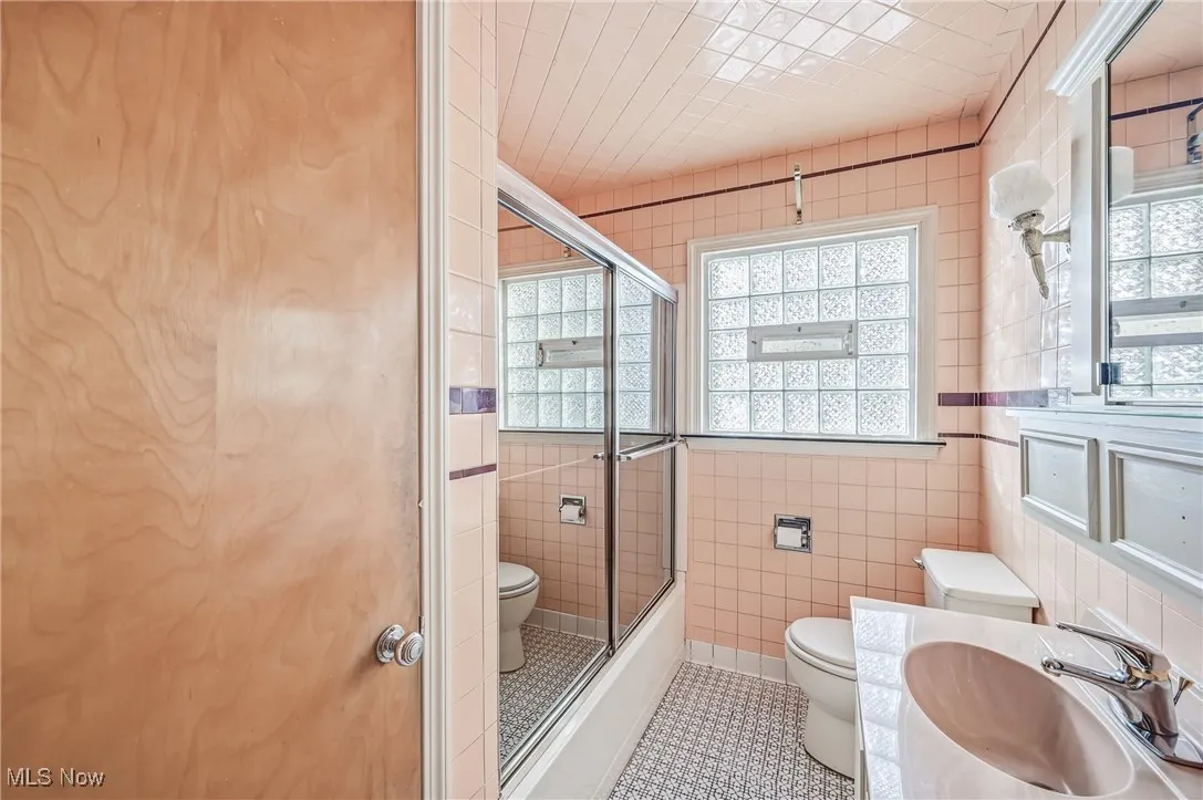 Bathroom featuring healthy amount of natural light, tile patterned floors, tile walls, vanity, and enclosed tub / shower combo