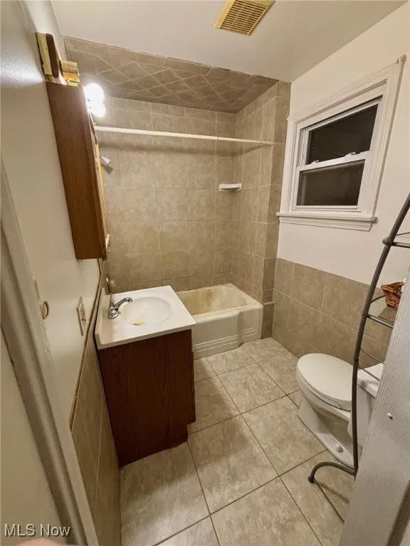 Full bathroom featuring tile walls, vanity, bathtub / shower combination, and light tile patterned floors