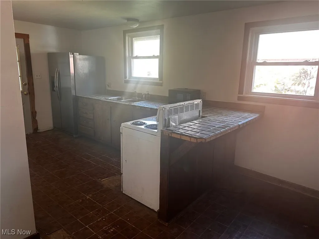 Kitchen featuring stainless steel fridge, tile counters, a peninsula, white range oven, and dark flooring