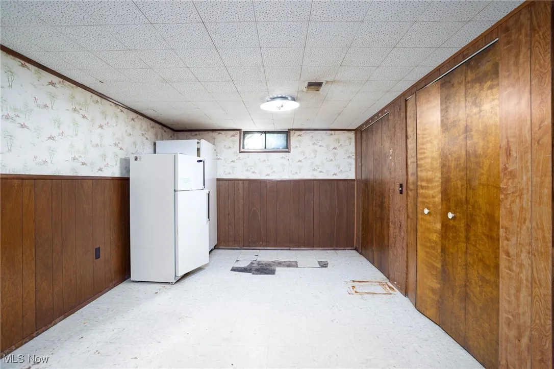 Basement featuring wood walls, a wainscoted wall, light floors, freestanding refrigerator, and wallpapered walls