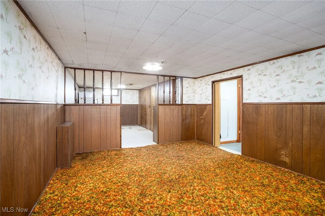 Unfurnished room with wallpapered walls, wainscoting, light carpet, and wood walls