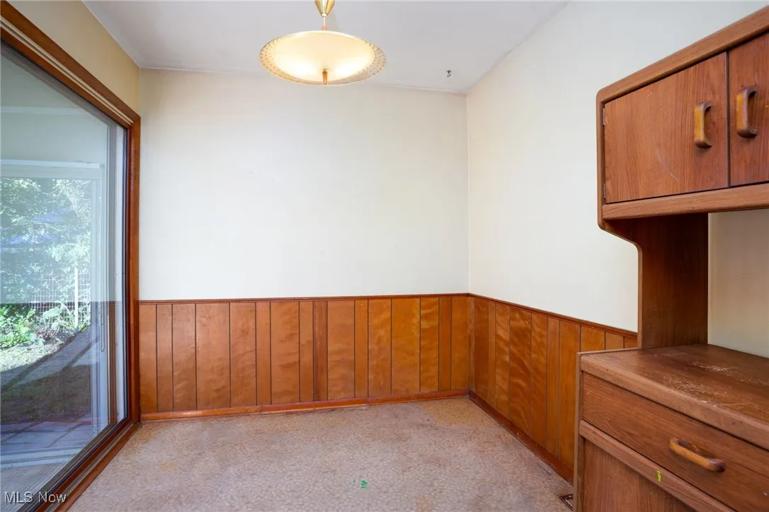 Unfurnished dining area with wood walls, wainscoting, and light carpet