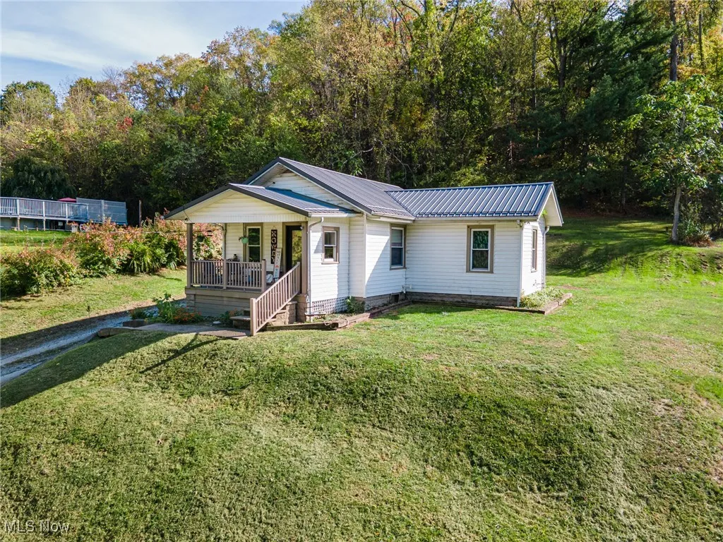 Bungalow-style home featuring a porch, a metal roof, a front lawn, and view of wooded area